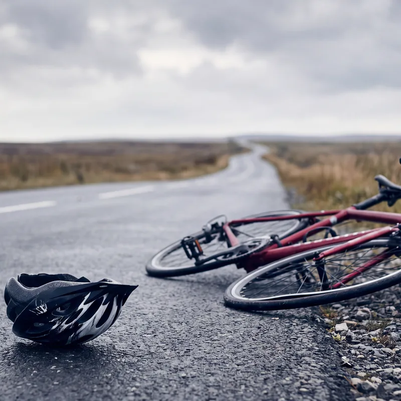 Crimson road bicycle with a bent wheel lying beside a rural road next to a helmet