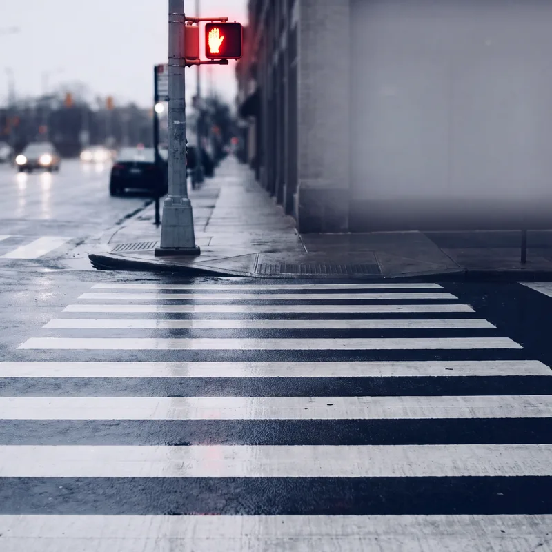 Crosswalk at dusk with approaching headlights and a crimson pedestrian signal